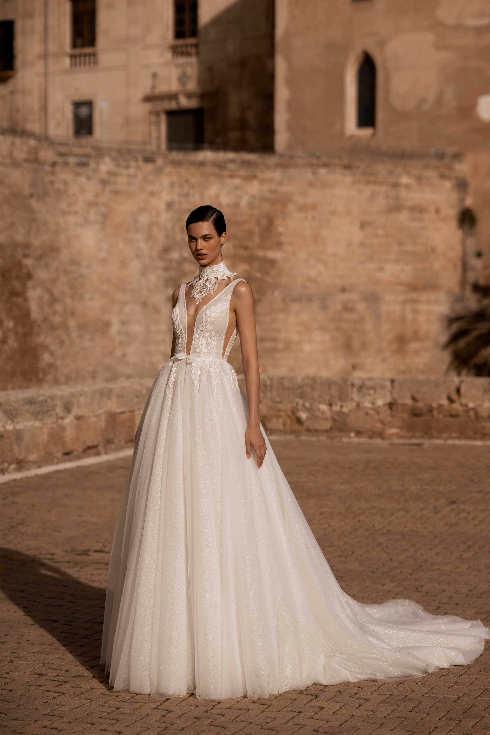 Abito da sposa Medeia Wonà con scollo profondo, applicazioni floreali sul corpetto, collo decorato e ampia gonna brillante, disponibile presso Altomare Sposa a Modena.