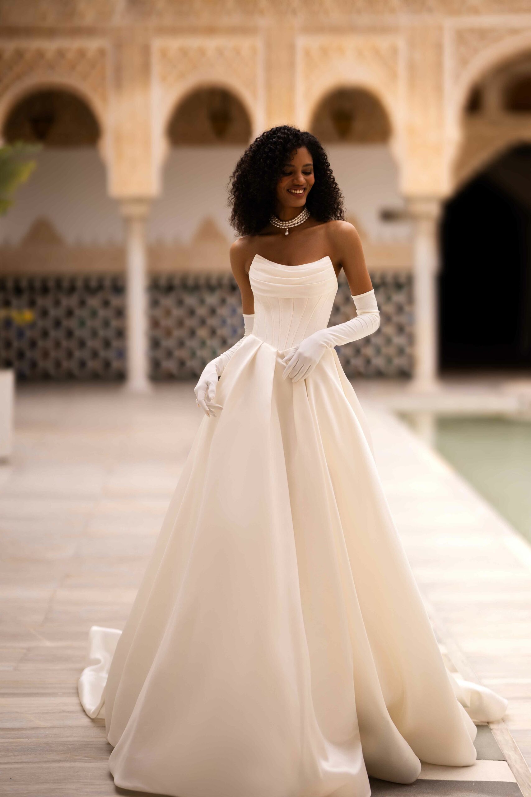 Abito da sposa Odette di Wonà con bustier drappeggiato, gonna ampia in mikado e lunghi guanti coordinati, indossato in un elegante chiostro storico, disponibile da Altomare Sposa a Modena.
