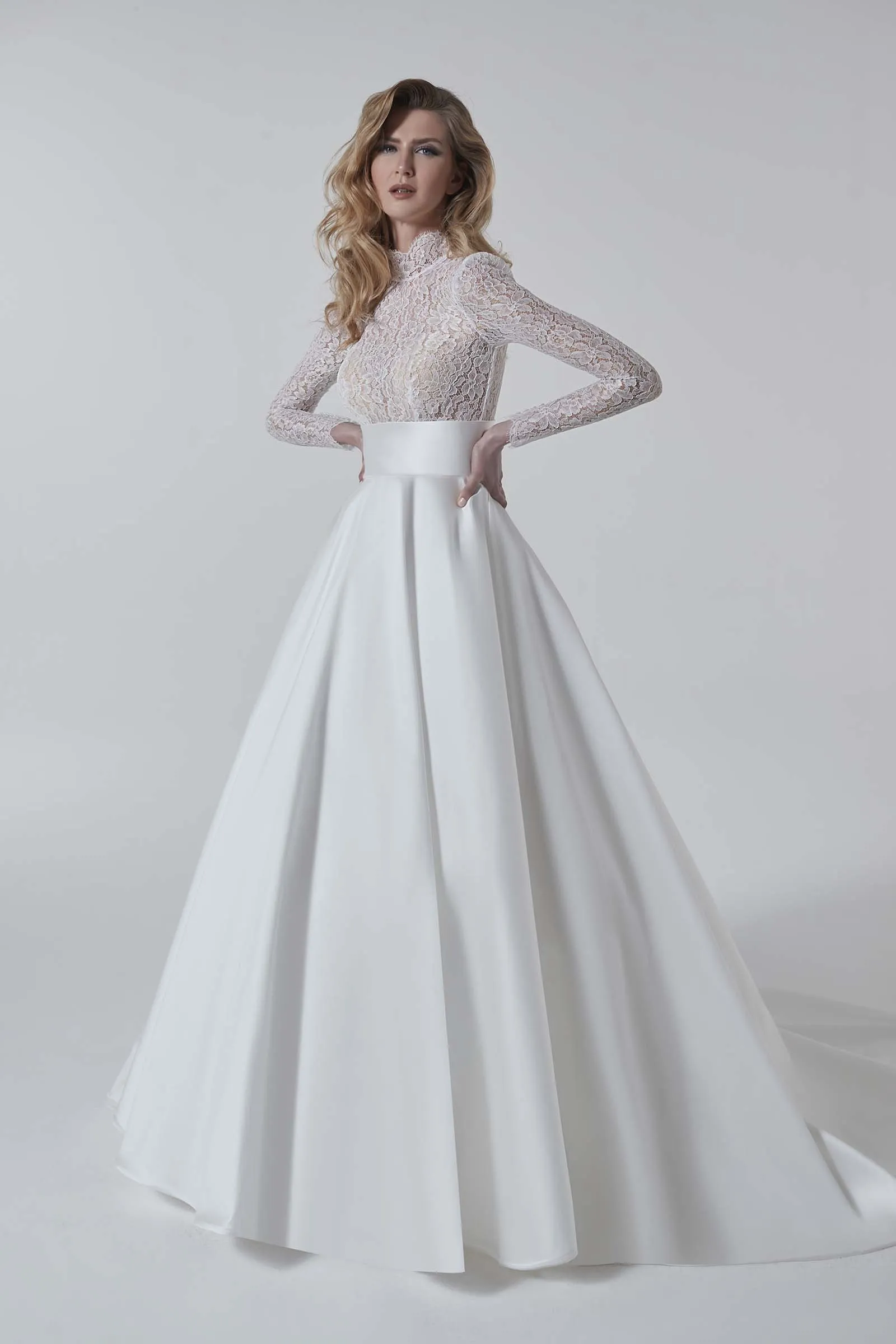Abito da sposa Anturio di Maison Signore con corpino in pizzo a maniche lunghe, collo alto e ampia gonna principesca in mikado, fotografato su sfondo neutro da studio.