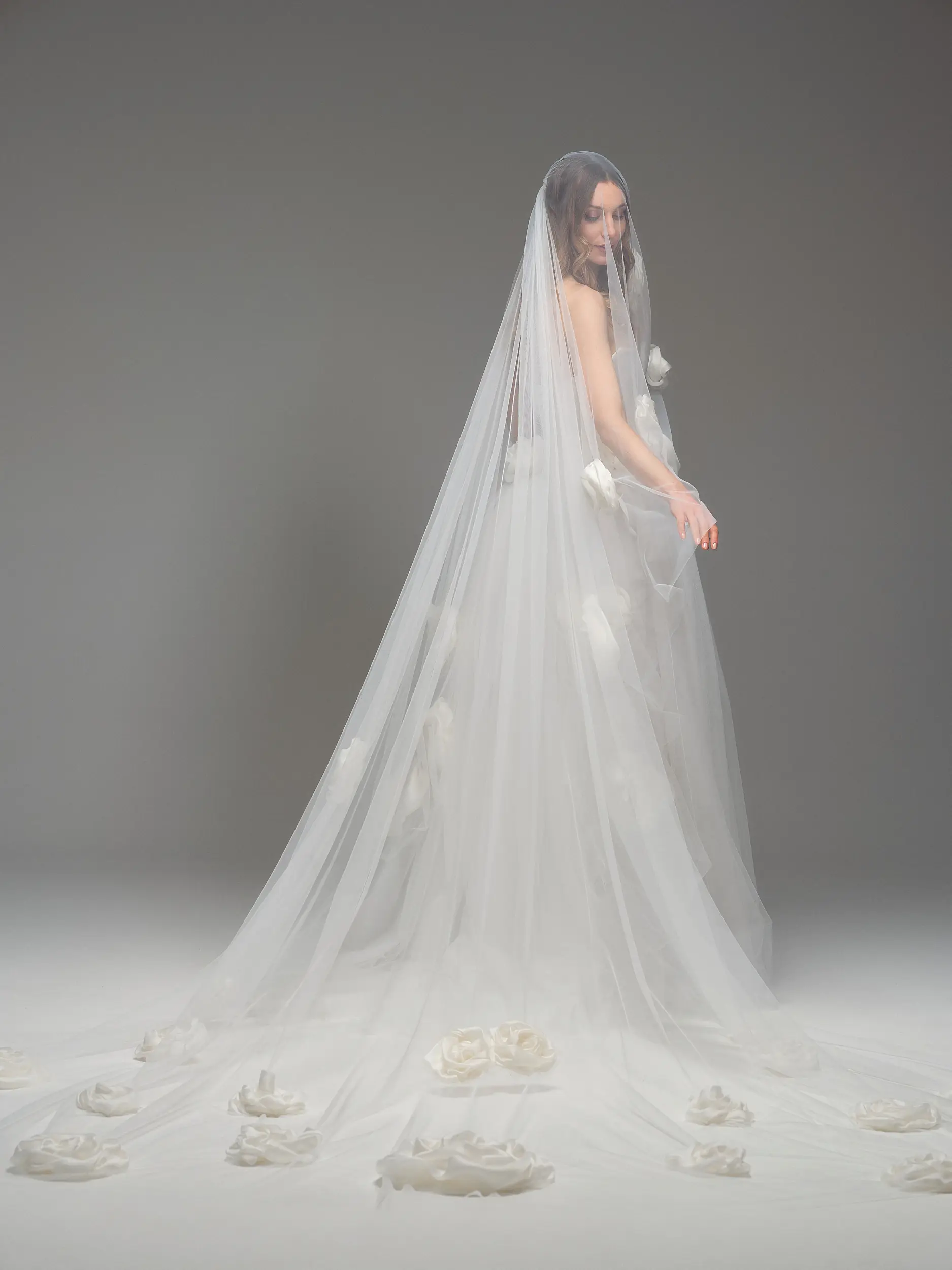 Abito da sposa Ibbie di Maria Pia con lungo velo in tulle decorato da dettagli floreali, silhouette romantica e strascico etereo, fotografato in studio su sfondo neutro, disponibile da Altomare Sposa a Modena.