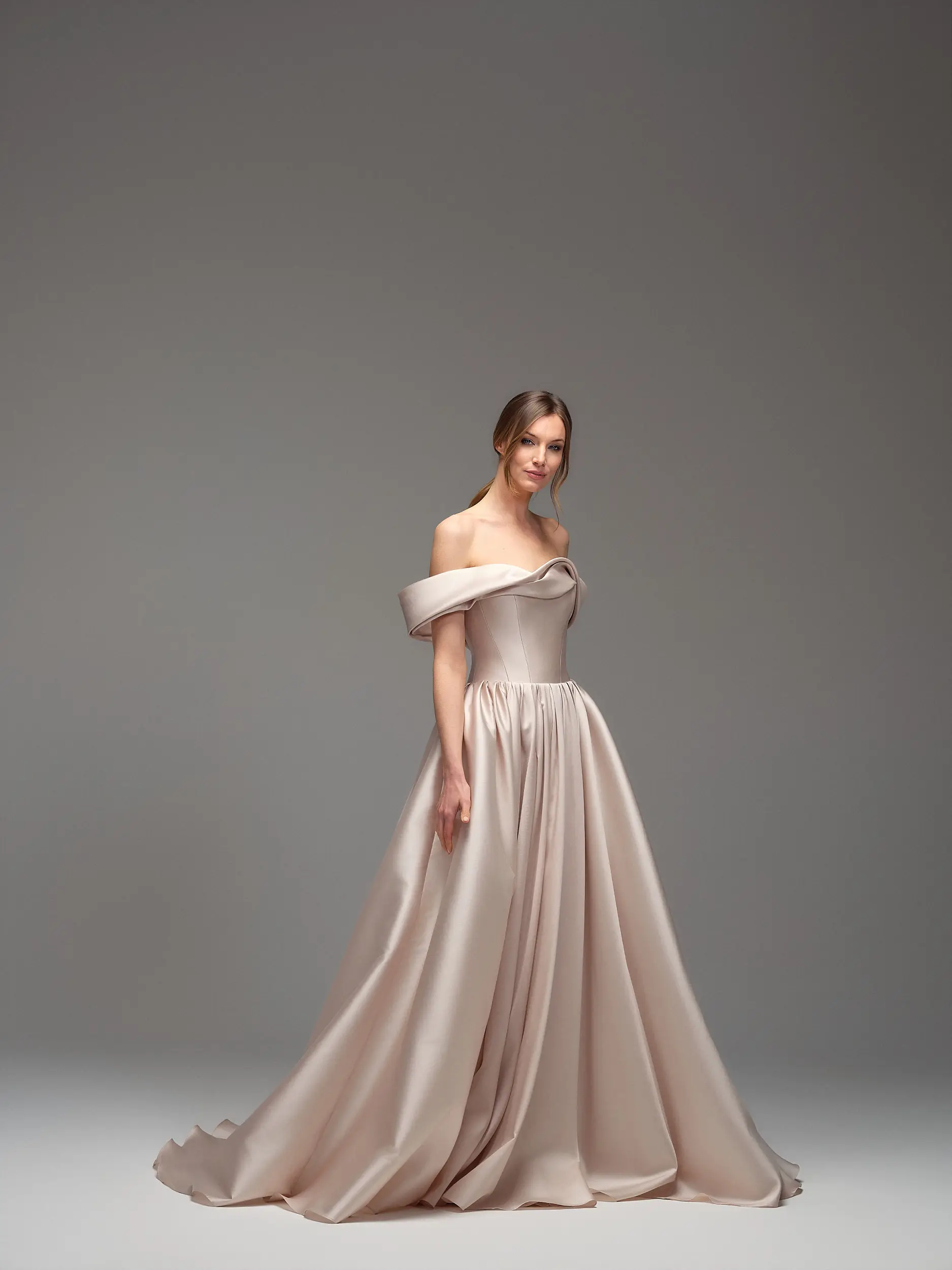 Abito Maria Pia Ilean con scollo off shoulder drappeggiato, bustier strutturato e ampia gonna satinata cipria, disponibile da Altomare Sposa atelier a Modena.