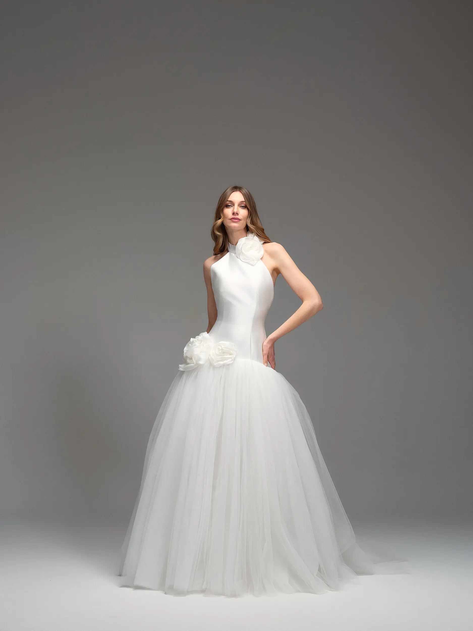 Abito da sposa Maria Pia Isolde con collo alto decorato da fiore, corpino liscio e ampia gonna in tulle bianco, disponibile da Altomare Sposa atelier a Modena.